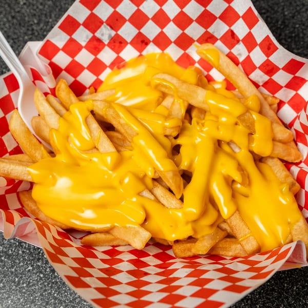 Mel's Hot Dogs' golden french fries generously covered with melted yellow cheese sauce in a red and white checkered paper tray.