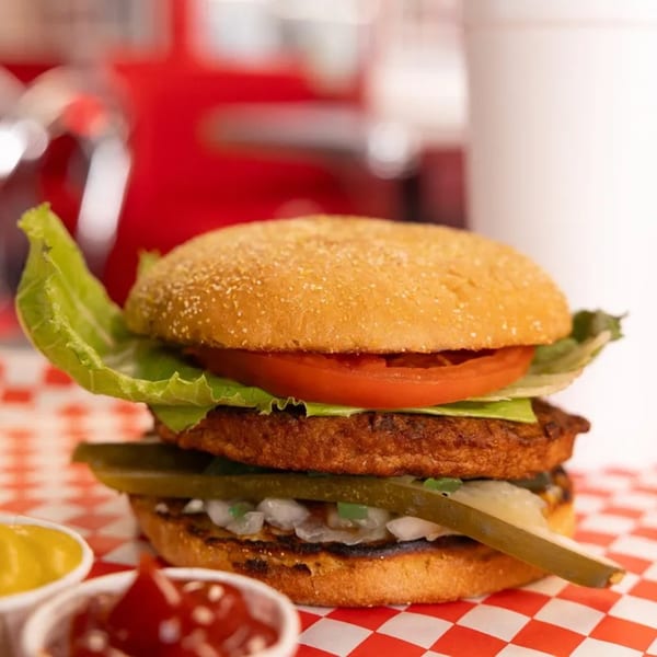 A Mel's Hot Dogs burger with lettuce, tomato, pickles, and onions, served with ketchup and mustard.