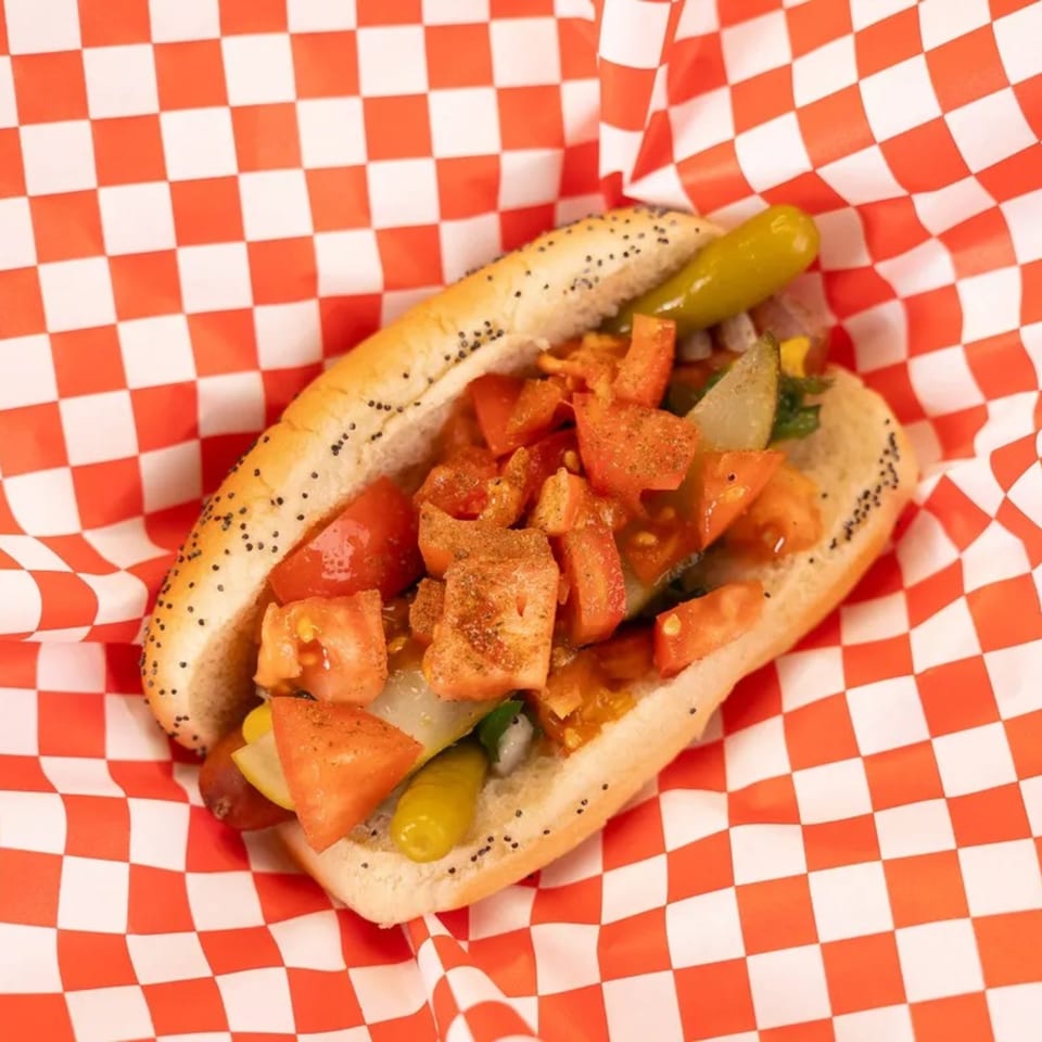 Mel's Hot Dog with diced tomatoes, pickles, and spices in a poppy seed bun.