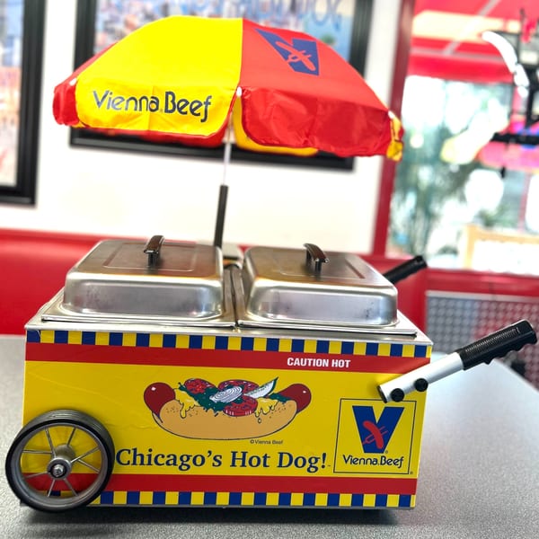 A miniature Vienna Beef hot dog cart with a red and yellow umbrella sits on a table.