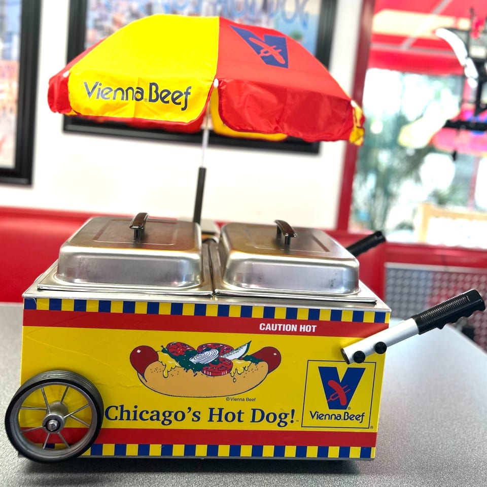 A miniature Vienna Beef hot dog cart with a red and yellow umbrella sits on a table.