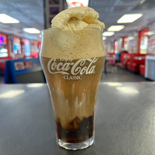 A Coca-Cola float with a scoop of vanilla ice cream in a branded glass at Mel's Hot Dogs.